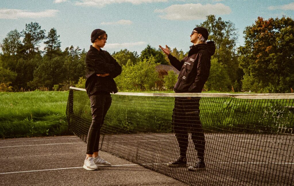 An image of two teenage boys standing on either side of a tennis net. 